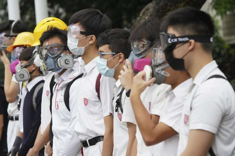 香港「反送中」運動，中學生牽起人鍊，不忘戴上防毒面具或口罩象徵抵抗警察暴力。（AP）