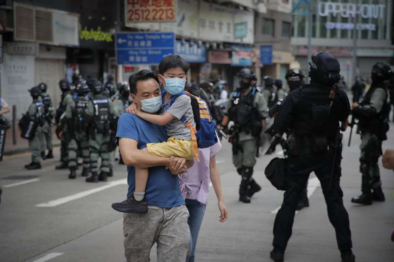 2020年7月1日,《國安法》陰影籠罩香港,一對父子走過嚴陣以待的防暴警察。(AP) 2020年7月1日,《國安法》陰影籠罩香港,一對父子走過嚴陣以待的防暴警察。(AP)