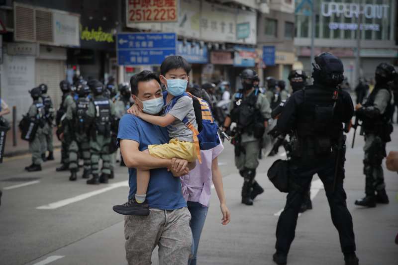 2020年7月1日，《國安法》陰影籠罩香港，一對父子走過嚴陣以待的防暴警察。（AP）